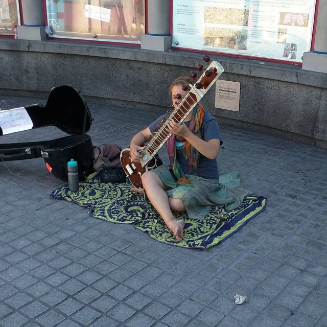 a woman is sitting on the ground playing the guitar