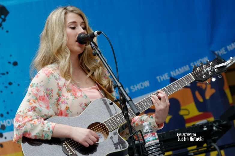 a woman standing in front of a microphone while holding a guitar