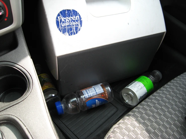 a bottle of liquid sits next to a cup and car cup holder