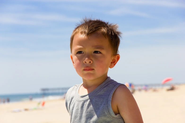 a boy is standing on the beach with a smirk on his face