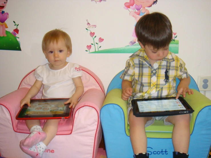 a  and a younger one sit on bean chairs holding electronic devices
