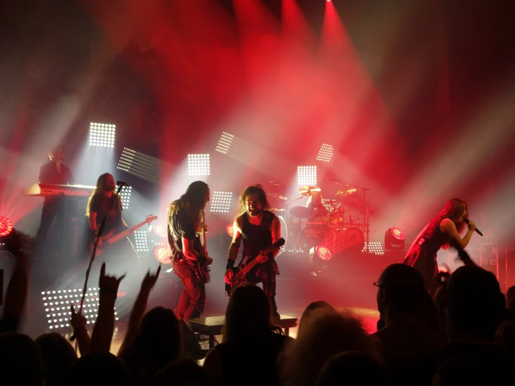 three women stand on stage, as the audience holds their arms in the air