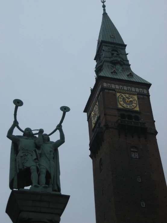 a statue stands in front of a tall clock tower