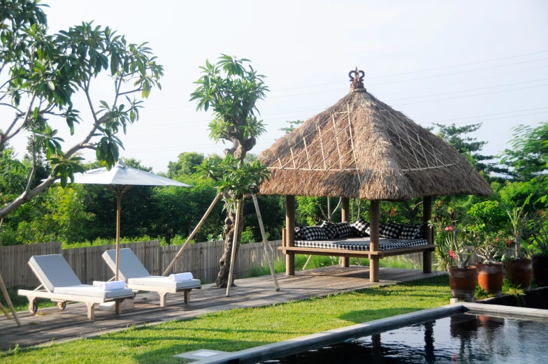 a thatched roof sits above a pool and chaise lounges