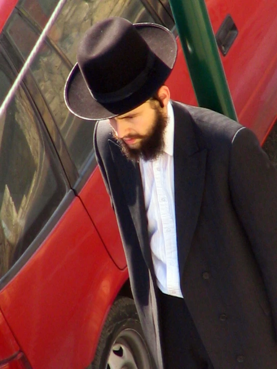 a man in a hat looking down near a red car