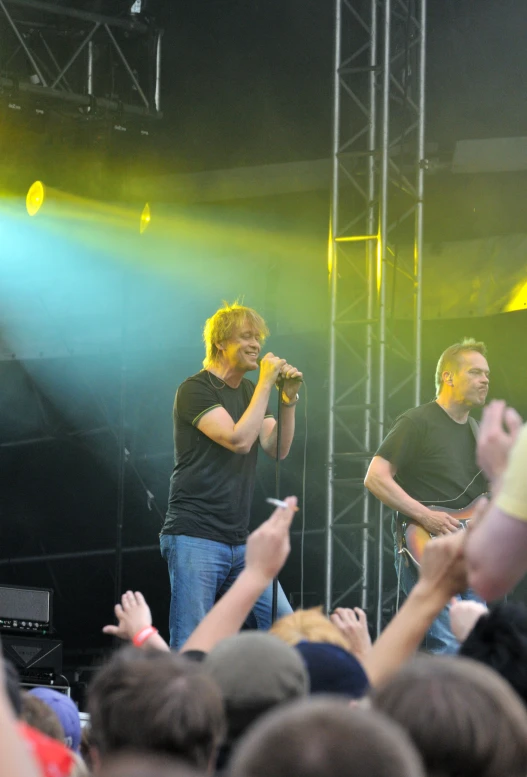 one man holding a microphone and other one wearing a black t - shirt