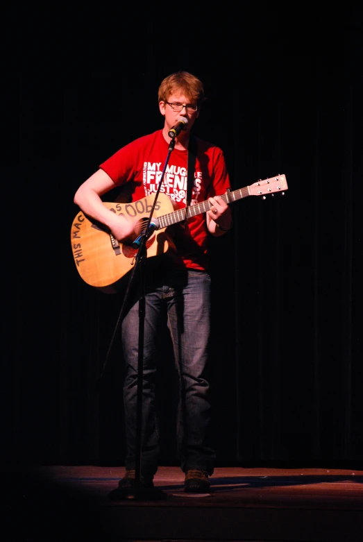 a man with glasses and a red shirt playing a guitar