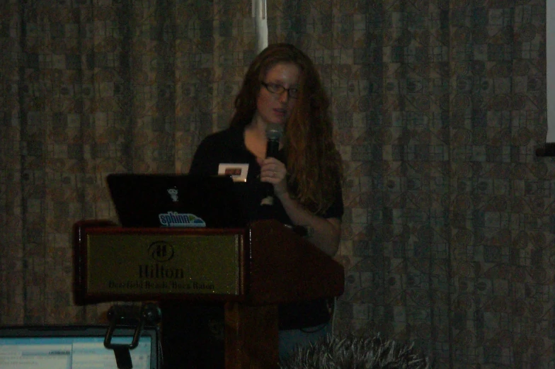 a woman stands at a podium talking on the computer