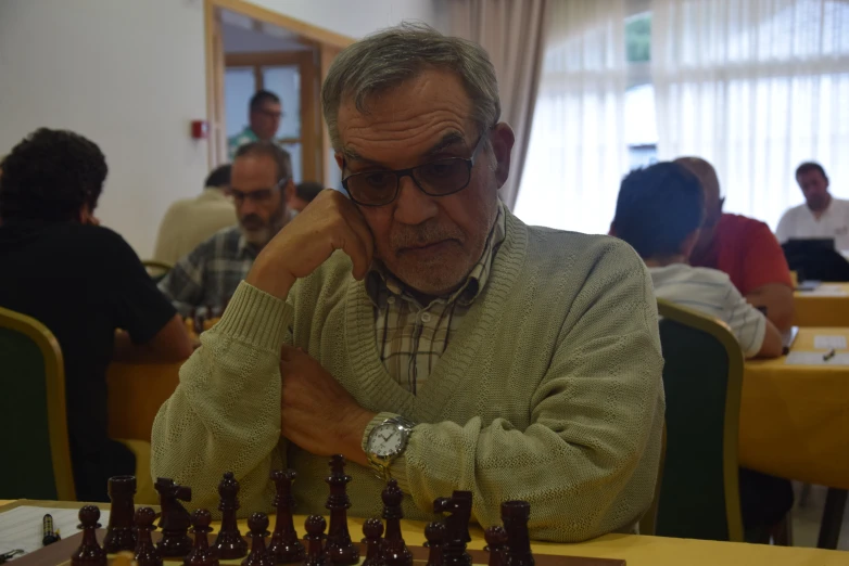 the man plays chess at a restaurant while others look on