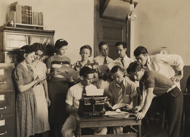 a group of people standing around a table with a typewriter