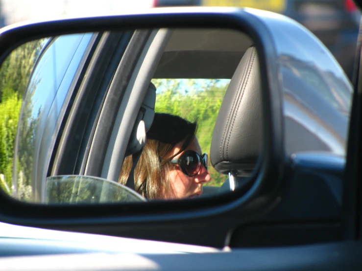 a woman sitting in a car while looking at the rear view mirror