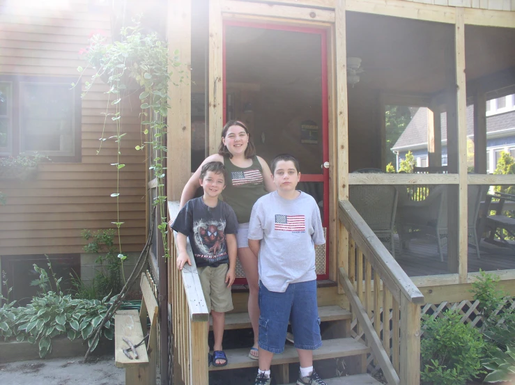 three children and their mom are standing outside of a cabin