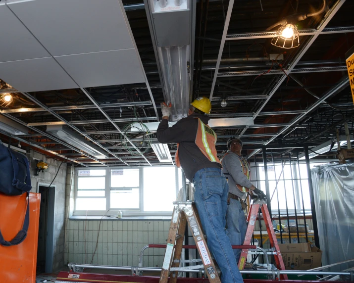 two construction workers are on ladders and in the background are lights