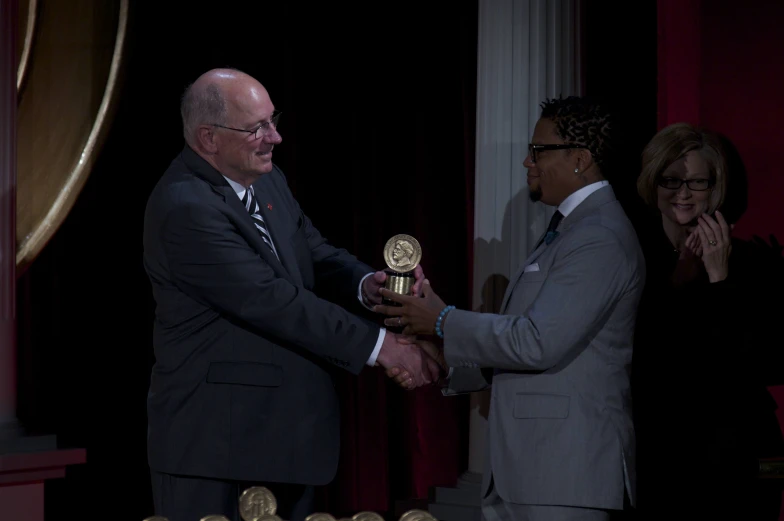 an older man in suit shaking another mans hand