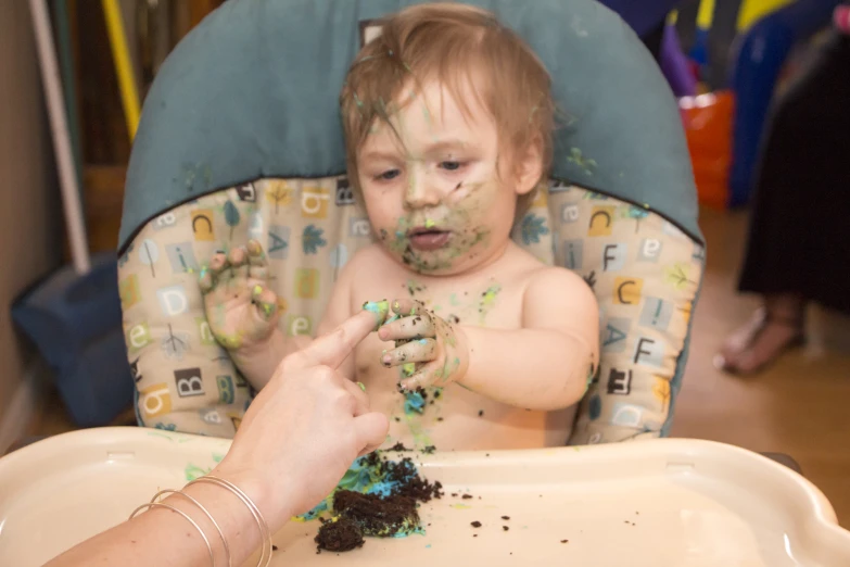 small child is in a high chair and he is eating dirt from the seat