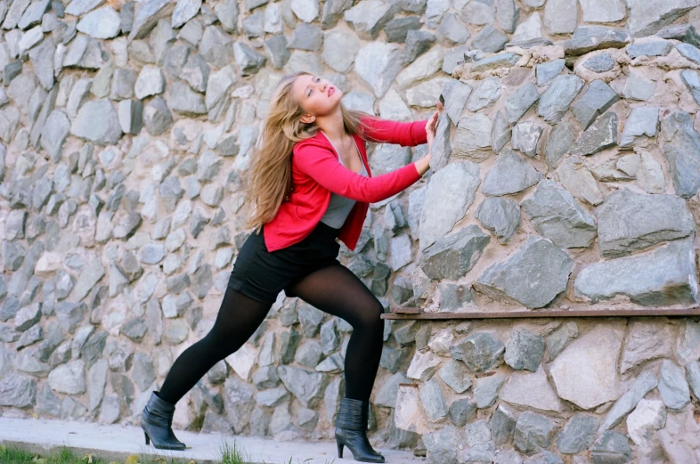 the woman is posing against a stone wall