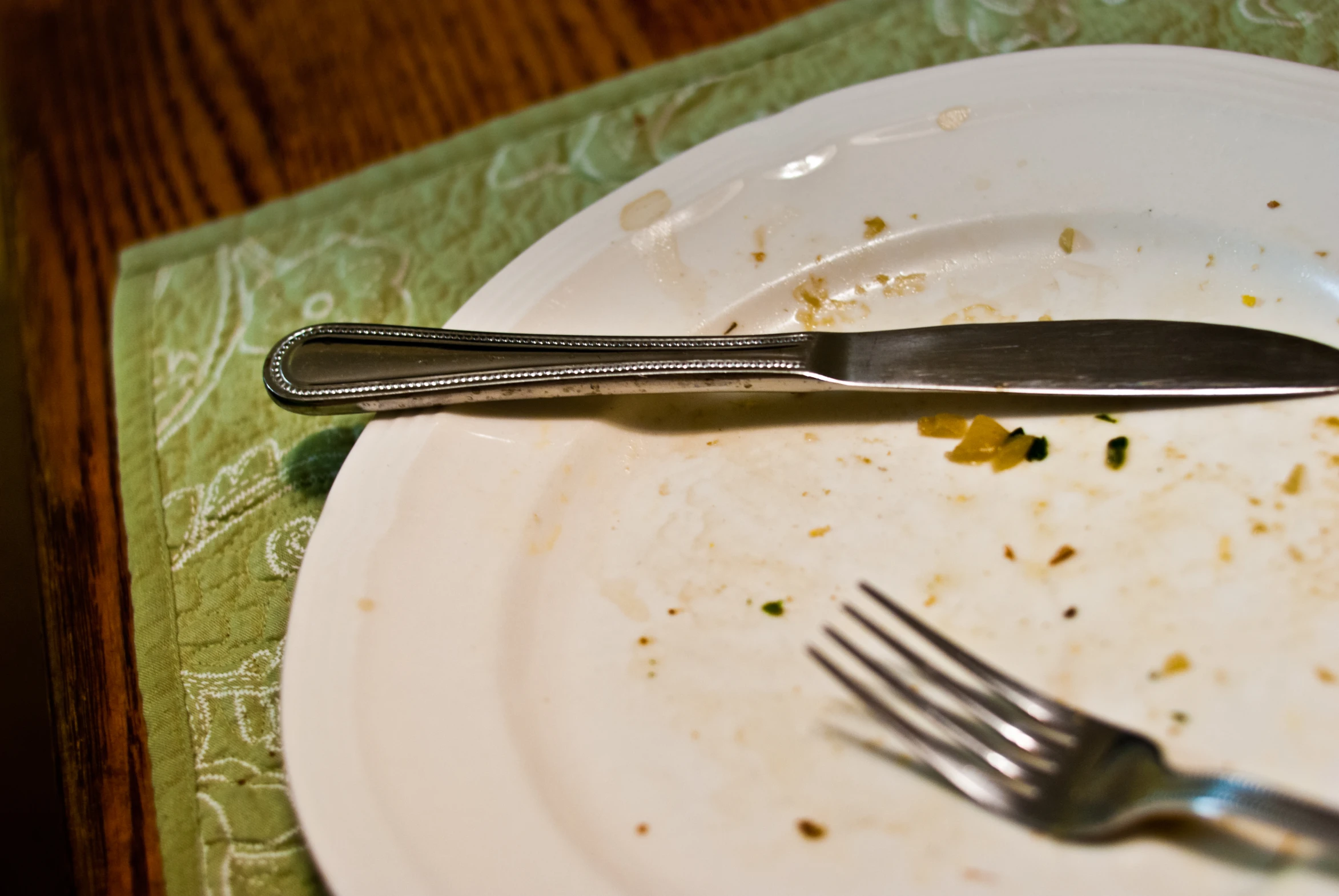 dirty fork and paper plate on green napkin with a crumby design