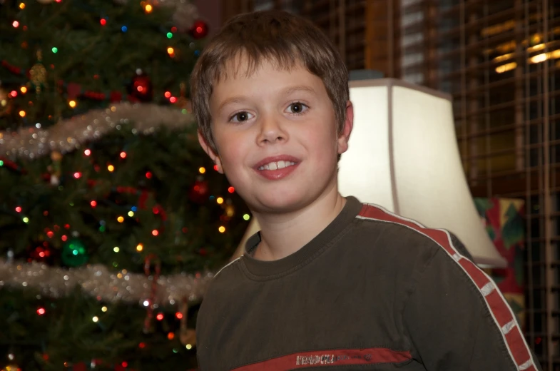 a boy that is standing up in front of a christmas tree