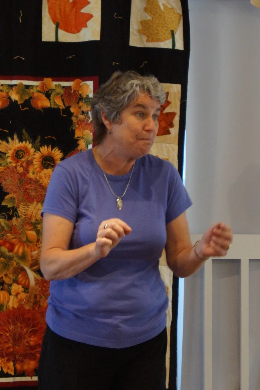 an older woman standing next to flowers wearing a purple shirt