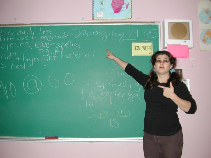 a woman pointing to a blackboard with a large amount of writing on it