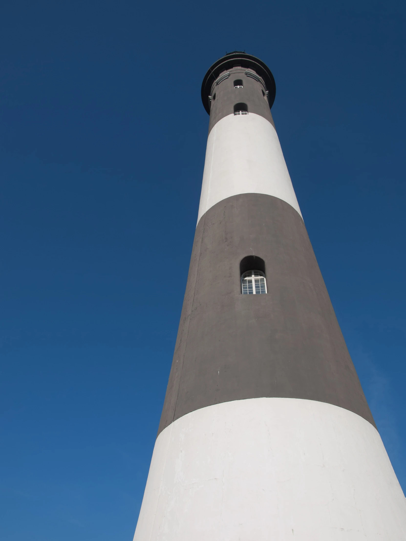 a tall white and black lighthouse with a sky background