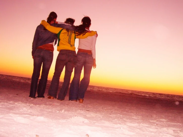 four people standing in the snow and one person wearing yellow is looking off into the distance