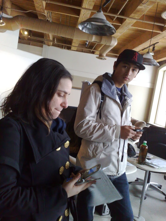 a man looking at a paper on his cell phone as a woman stands by her