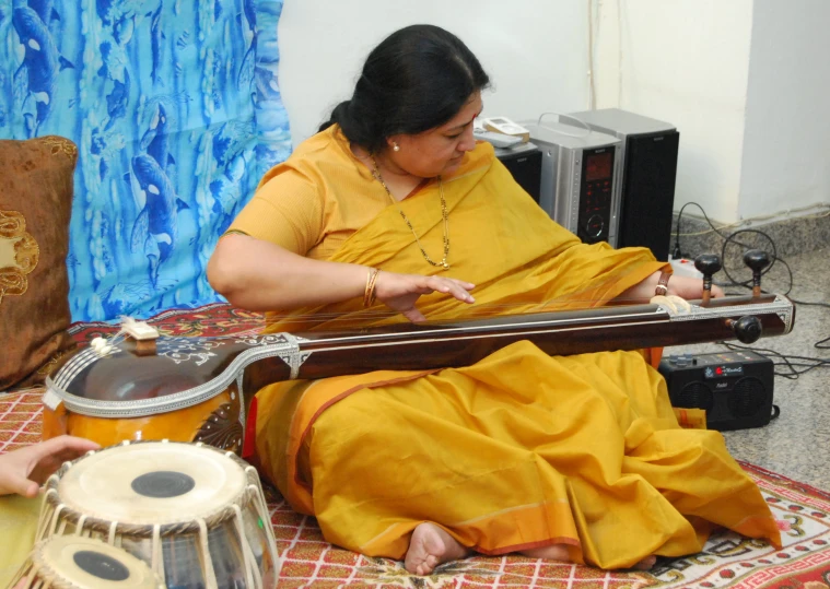 a woman playing music on a drum with a person standing near by