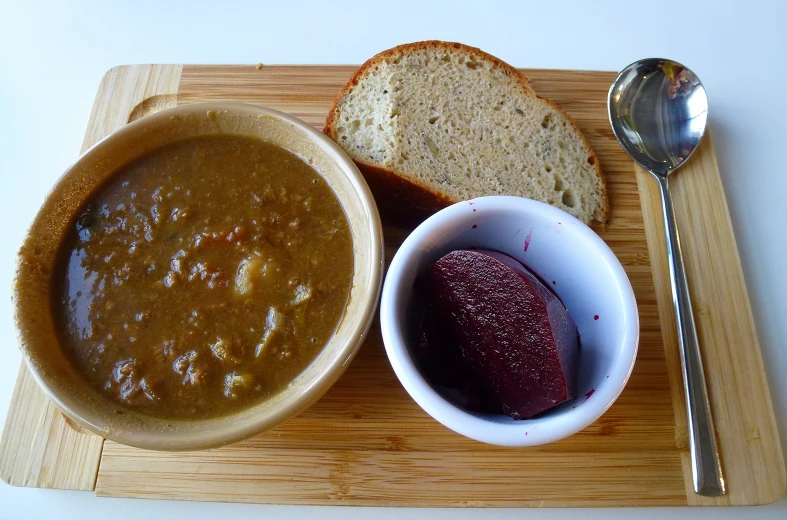 a wooden plate topped with a bowl of soup next to bread