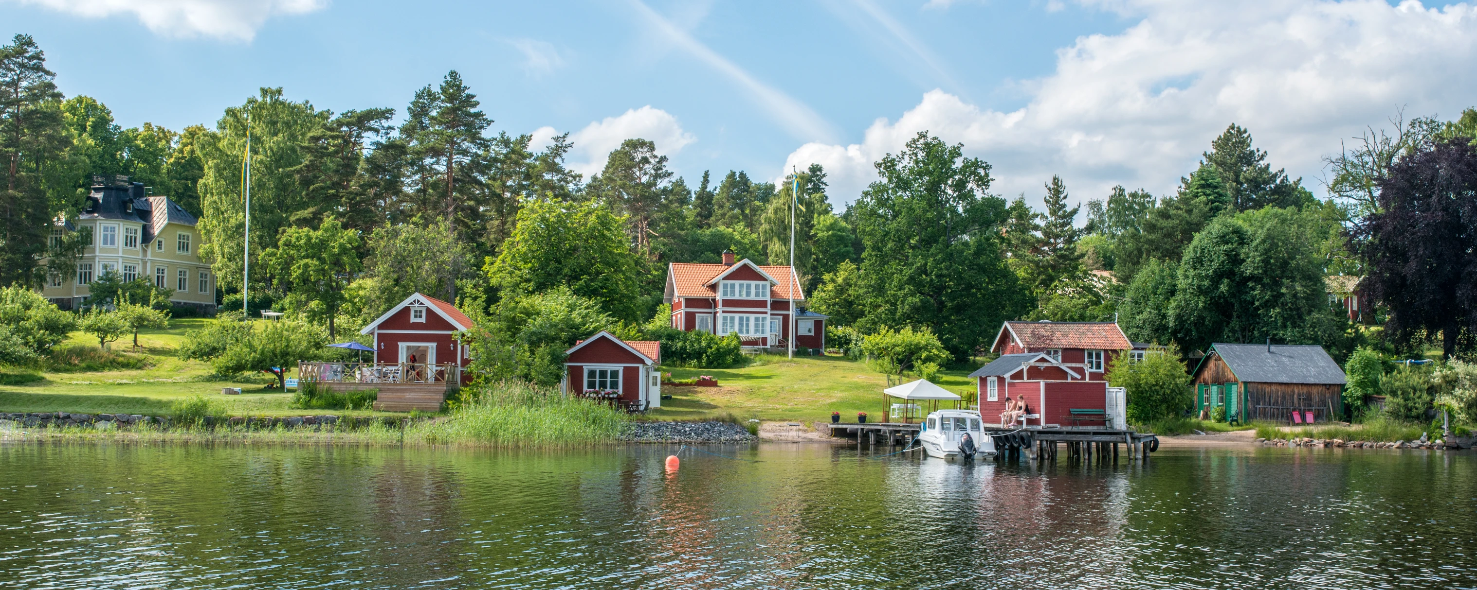 red cottages on a lake in the summer with lush trees surrounding them