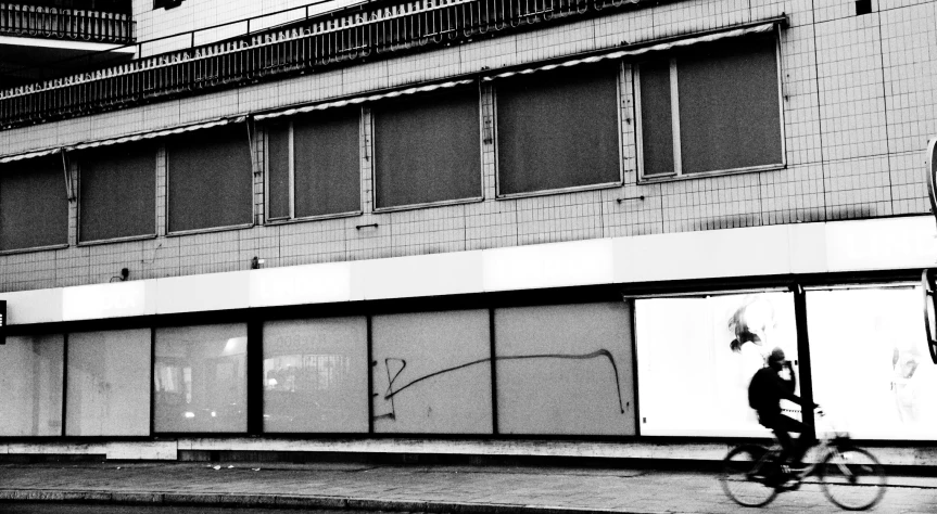 a black and white image of a woman walking her bike past a building