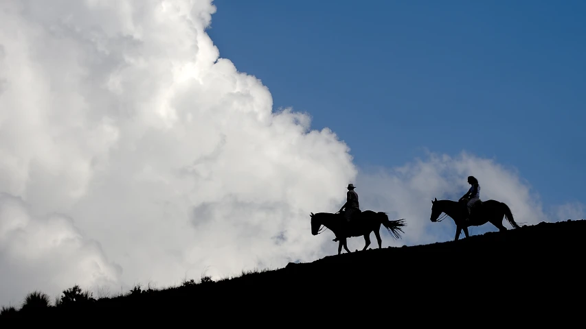 two silhouettes of people riding on the back of horses