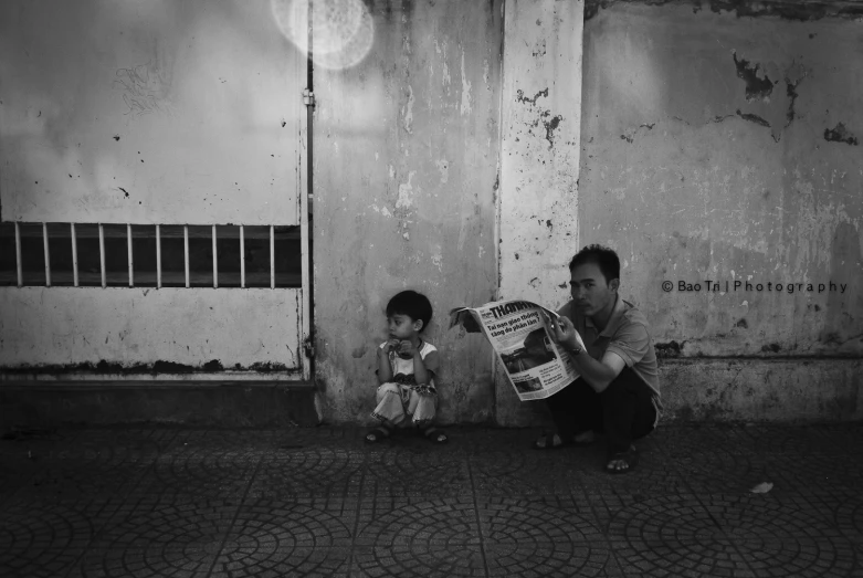 a man kneeling down next to a child holding a newspaper