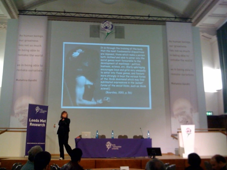 a woman speaking at an event with a projected picture on the wall