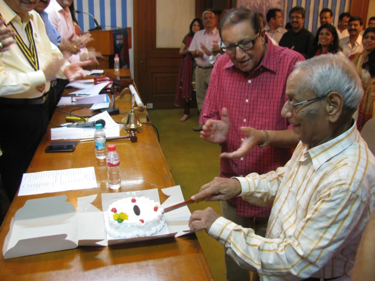 two older people celeting with cake, candles and people around