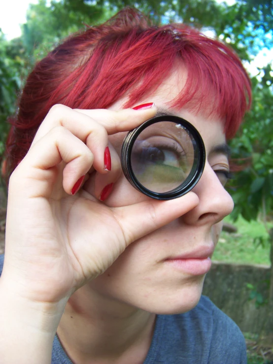 a woman in blue shirt with red nails and black round glasses looking through a lens