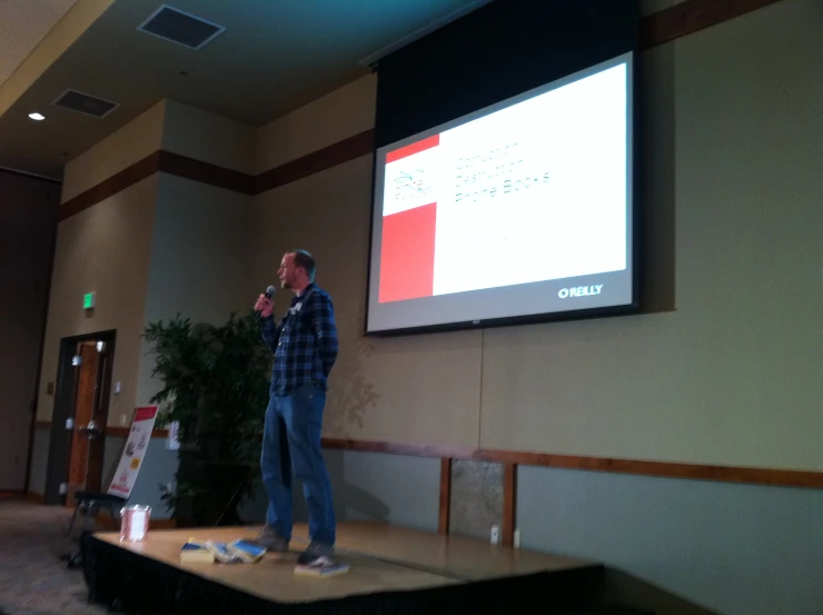 man stands on stage giving a presentation in front of people