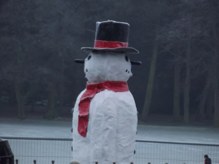 a snowman with red ribbon and hat in front of fence