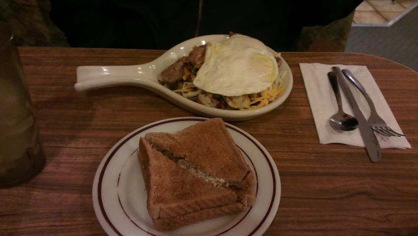 a bowl of scrambled egg, sandwich and er and spoon on a table