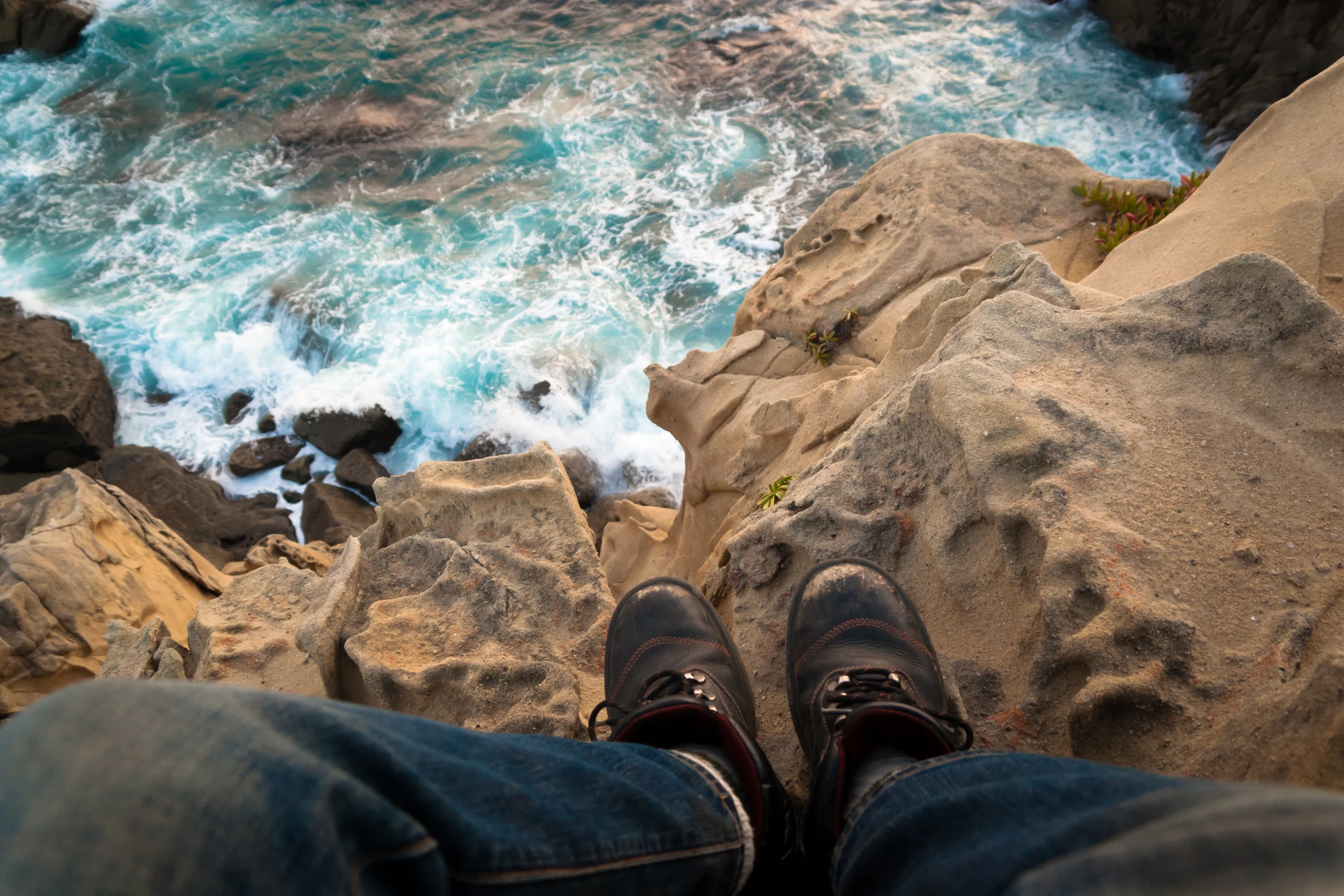 a person sitting on the edge of a cliff by the ocean