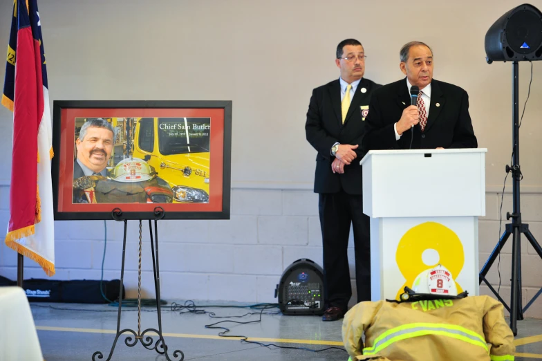 two men standing at a podium with a tv behind them