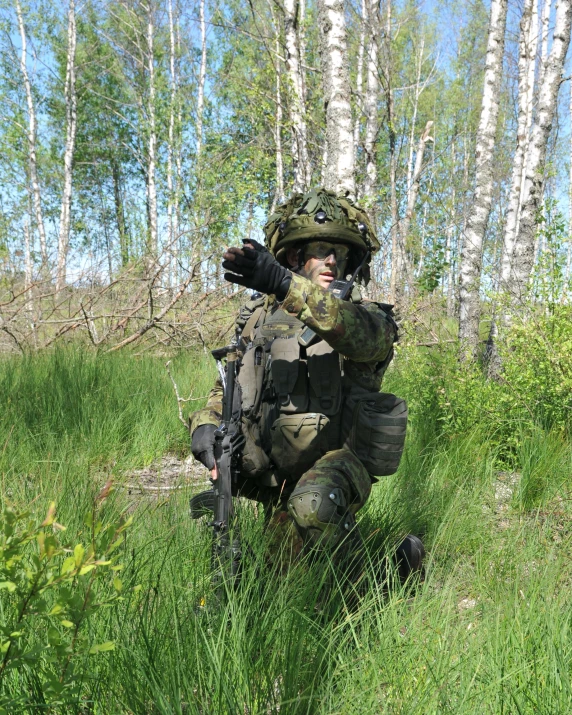 the soldier is in camouflage crouching in the brush