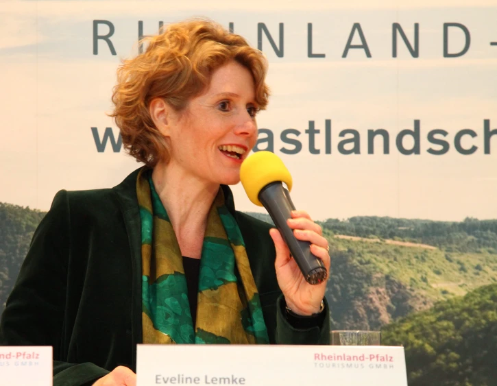 woman in green suit talking into a microphone at press