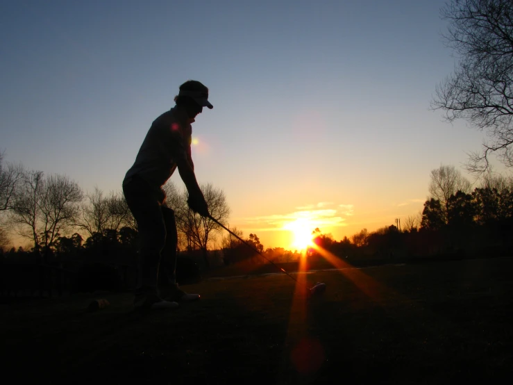 a man golf is silhouetted in the sun setting