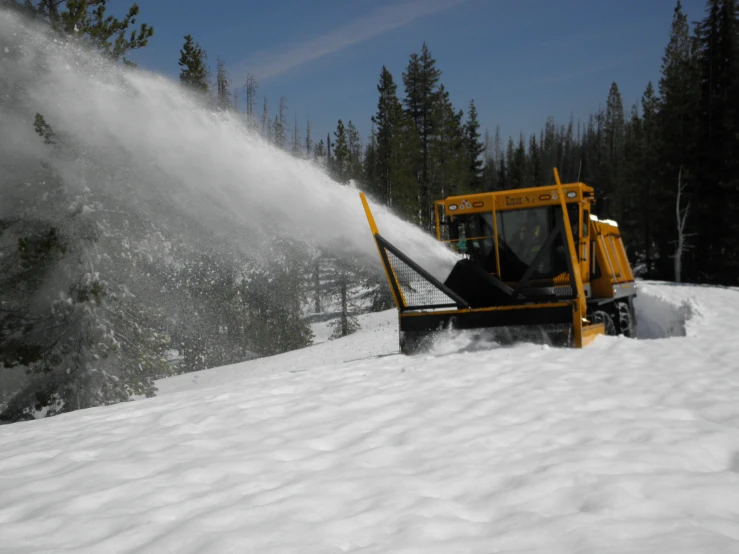 a yellow snow thrower spraying out snow on the slope