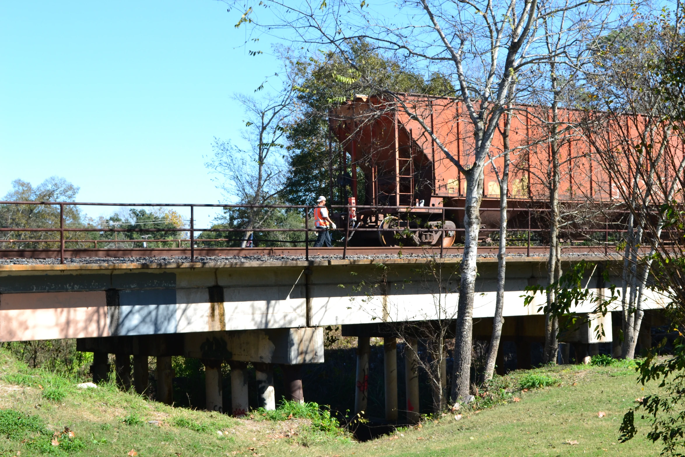 a man walks across a bridge with a train behind him