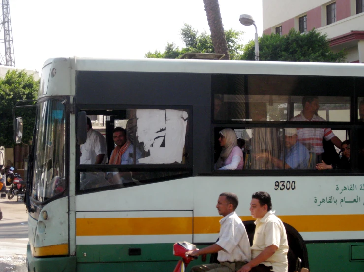 two men on a bicycle sit beside a bus