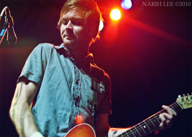 a man holding a guitar while standing in front of a microphone