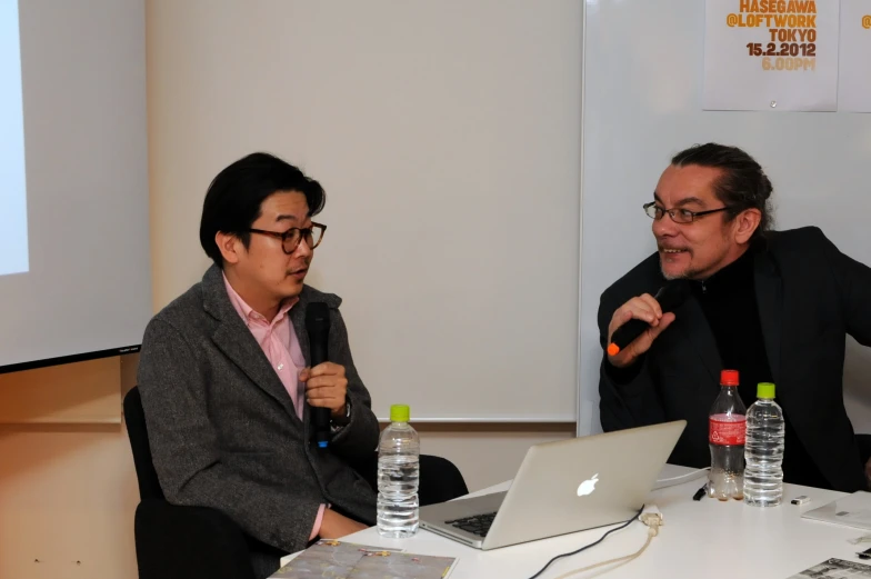 two people sitting in front of a laptop computer on a desk