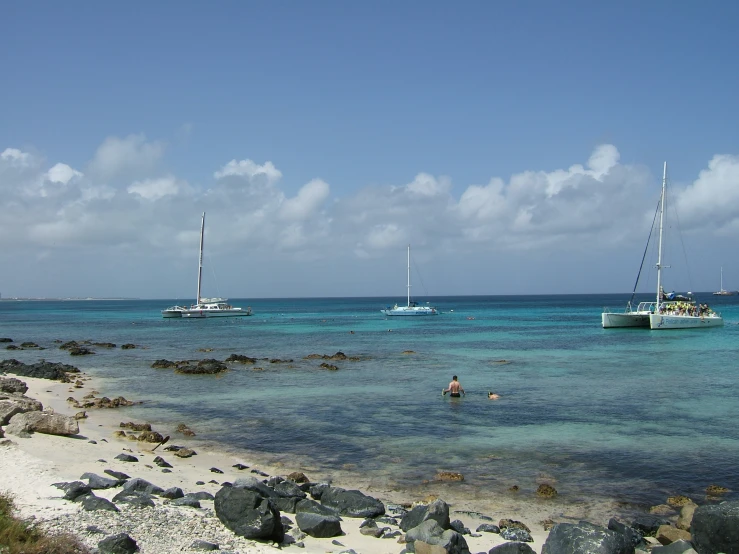 two sailboats on clear blue water near rocks